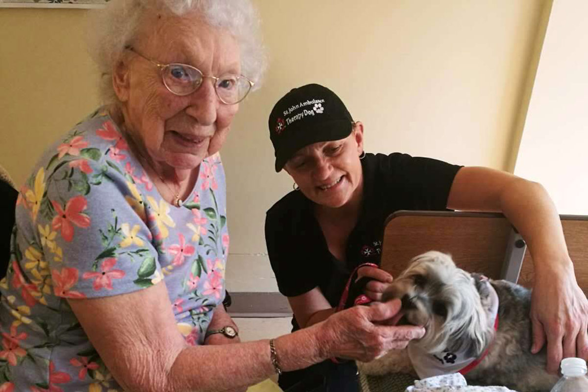Elderly woman playing with puppy with Solana from St. John's Ambulance Therapy Dog service